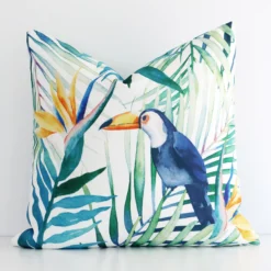Toucan and leaf printed cushion cover in front of a white wall. It has a square size and is made from an outdoor material.