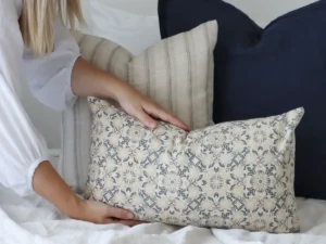 A lady is arranging cushions and is about to place a cushion in front of the collection.