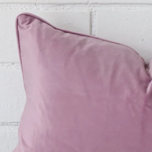A zoomed in photo of the corner of a lavender cushion that has velvet fabric and a rectangle size.