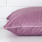 A lavender cushion arranged sideways in front of a wall. The large size and velvet fabric are shown and the seams are clearly visible.