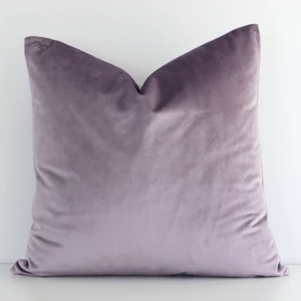 Lavender solid-coloured cushion cover in front of a white wall. It is square-shaped and is made from a velvet material.