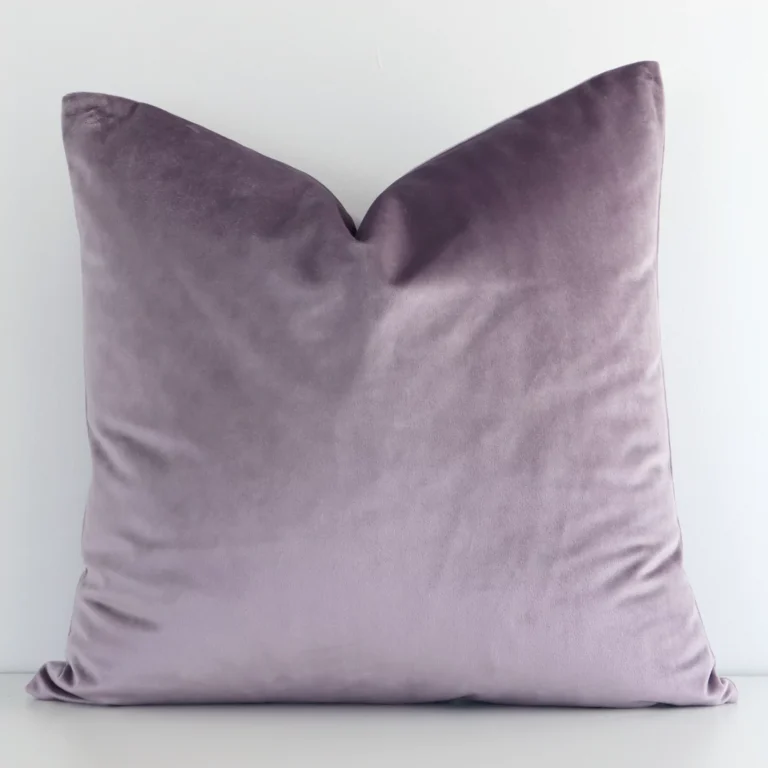 Lavender solid-coloured cushion cover in front of a white wall. It is square-shaped and is made from a velvet material.