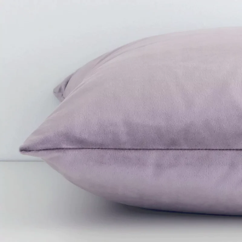 Close side shot of this lavender velvet cushion cover. The viewpoint shows how the square design and solid-coloured finish meet along its edge.