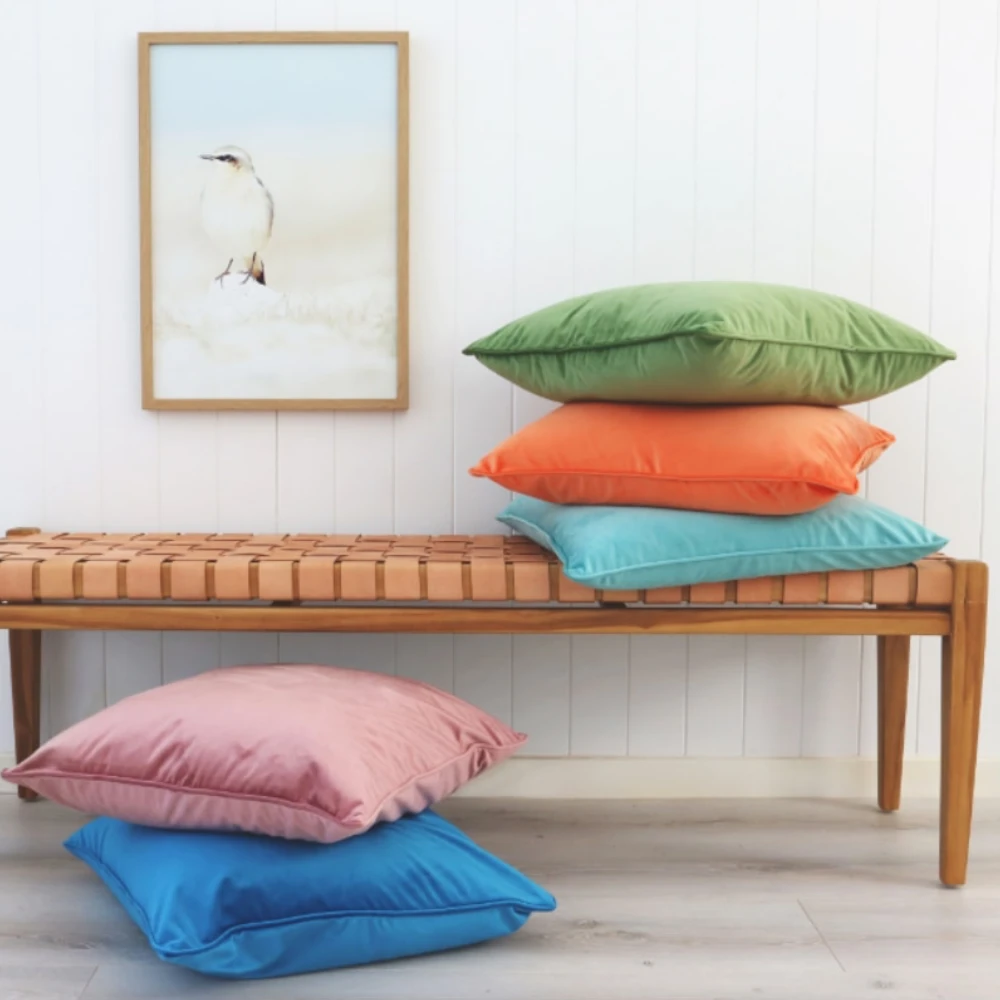 A leather and wood bench seat with two stacks of colourful cushions.