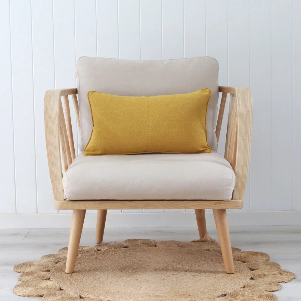 A light armchair in the middle of a room with a mustard cushion.