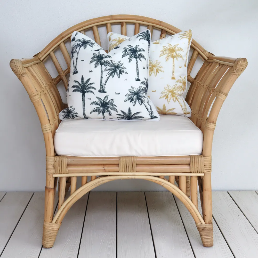 A light coloured arm chair against a wall has some palm tree cushions on it.
