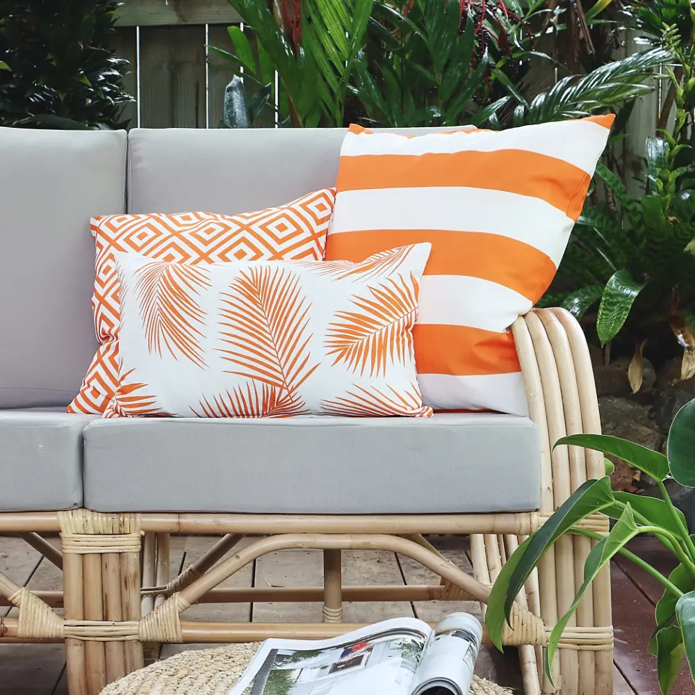 A light coloured setting with three orange outdoor cushions in its corner.