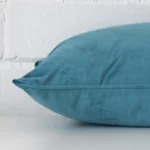 A teal cushion cover is laid flat. This angle shows the side of the velvet fabric and its rectangle shape.