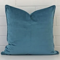 A velvet large cushion cover that is shown vertically against a brick wall. It has a wonderful teal colour.
