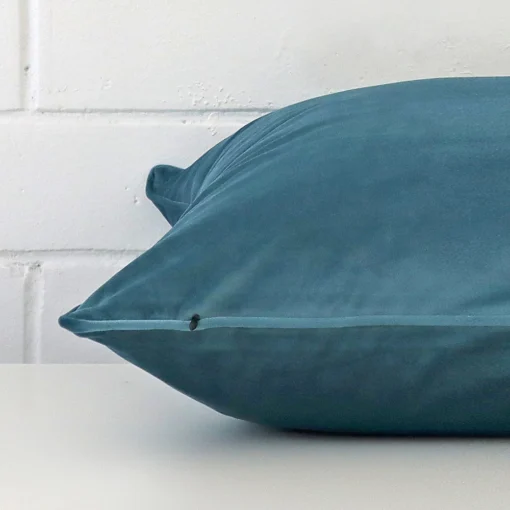 Large cushion in teal colour laying flat. The viewpoint highlights the seams of the velvet fabric.