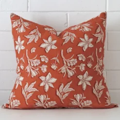 Rust floral cushion leans elegantly against a brick wall. It has been crafted from a high quality linen material and has a large size.