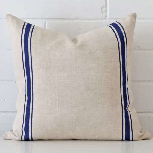 A brick wall that has a striped blue cushion cover positioned in front of it. It has an exquisite linen material and a lovely square shape.