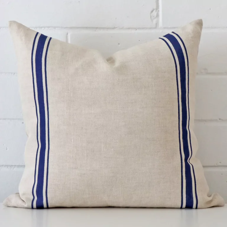 A brick wall that has a striped blue cushion cover positioned in front of it. It has an exquisite linen material and a lovely square shape.
