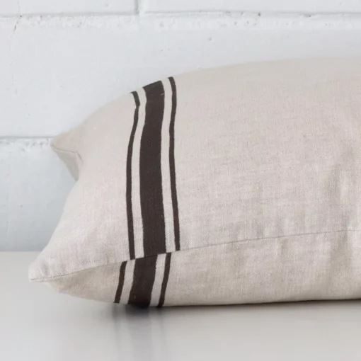 A side shot of a striped linen cushion cover. The angle shows the edge of the rectangle shape and the charcoal tone.