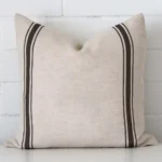 Charcoal striped cushion leans elegantly against a brick wall. It has been crafted from a high quality striped material and has a square shape.