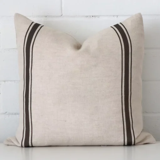 Charcoal striped cushion leans elegantly against a brick wall. It has been crafted from a high quality striped material and has a square shape.