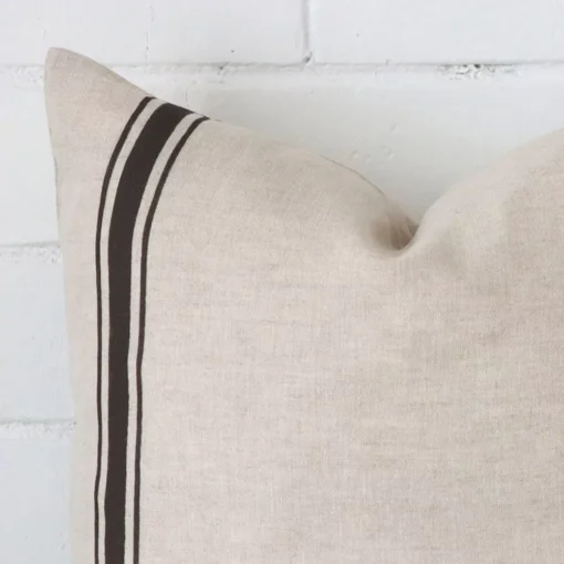 Enlarged shot of the corner of this square striped cushion cover in charcoal colour is shown against a brick wall. The image shows the quality and craftsmanship of the linen material.