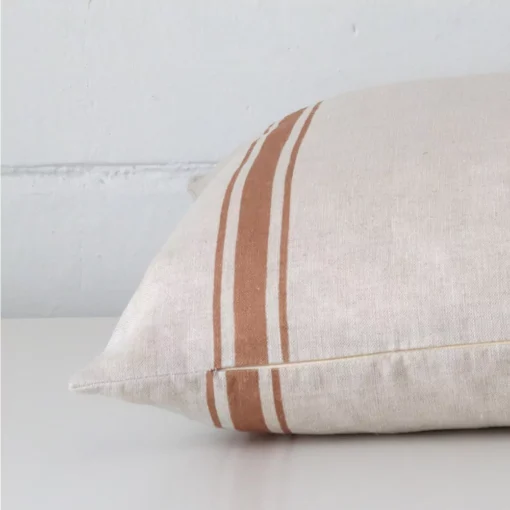 A rectangle linen cushion positioned flat to show its seams. The terracotta colour and striped design are visible as is the seam between the panels.
