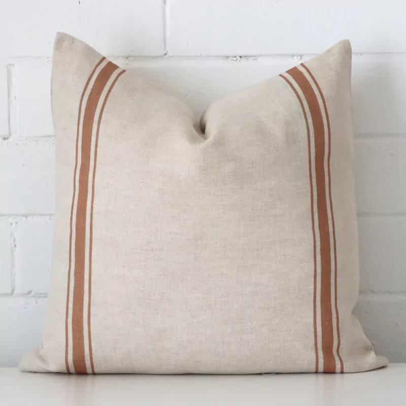 lyla-linen-terracotta-striped-cushion-cover-sc1004-45 A pretty striped linen cushion cover is shown against a brick wall. It features a square shape and a terracotta colour finish.
