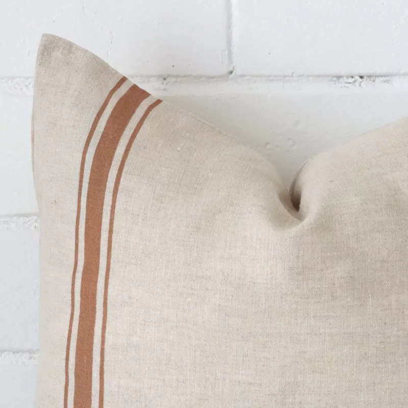 A linen square cushion’s corner has been enlarged in this shot. The detail of the striped design and terracotta colour are visible.