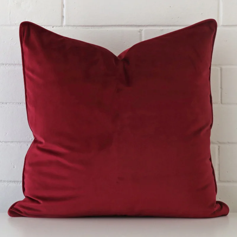 maroon-velvet-cushion-cover-55cm-x-55cm-sc771-55b A large cushion in a delightful maroon tone rests against a white wall. The velvet material appears to be of exceptional quality.