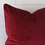 A very close image of the corner of a velvet cushion.The finer detail of the large shape and maroon colour are visible.