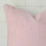 A macro image of the top left corner of this linen cushion. It is possible to see the finer detail of the square shape and baby pink colour.