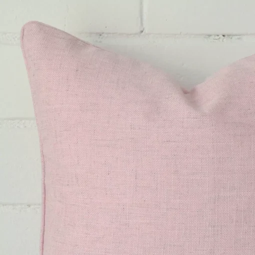 A macro image of the top left corner of this linen cushion. It is possible to see the finer detail of the square shape and baby pink colour.