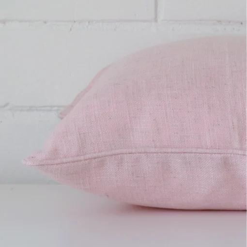 Baby pink cushion cover laid on its back side. The image shows a side-on view of the linen material and its square dimensions.