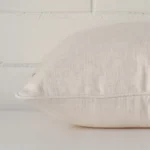 A cream cushion arranged sideways in front of a wall. The square size and linen fabric are shown and the seams are clearly visible.
