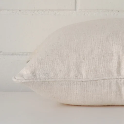 A cream cushion arranged sideways in front of a wall. The square size and linen fabric are shown and the seams are clearly visible.