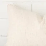 Enlarged shot of the corner of this rectangle cushion cover in cream colour is shown against a brick wall. The image shows the quality and craftsmanship of the linen material.