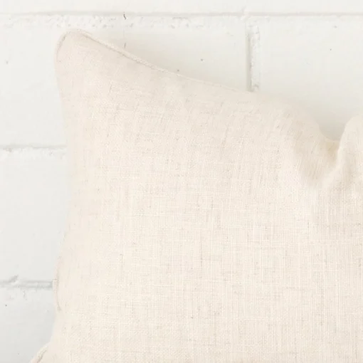 Enlarged shot of the corner of this rectangle cushion cover in cream colour is shown against a brick wall. The image shows the quality and craftsmanship of the linen material.