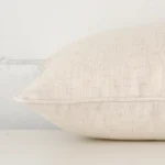 A linen cream cushion cover shown laying on its side. The edge of its rectangle size is shown.