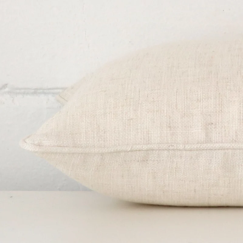 A linen cream cushion cover shown laying on its side. The edge of its rectangle size is shown.
