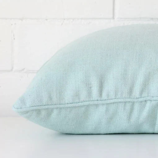 A square mint cushion cover laying flat. This viewpoint highlights the linen fabric from a side position.