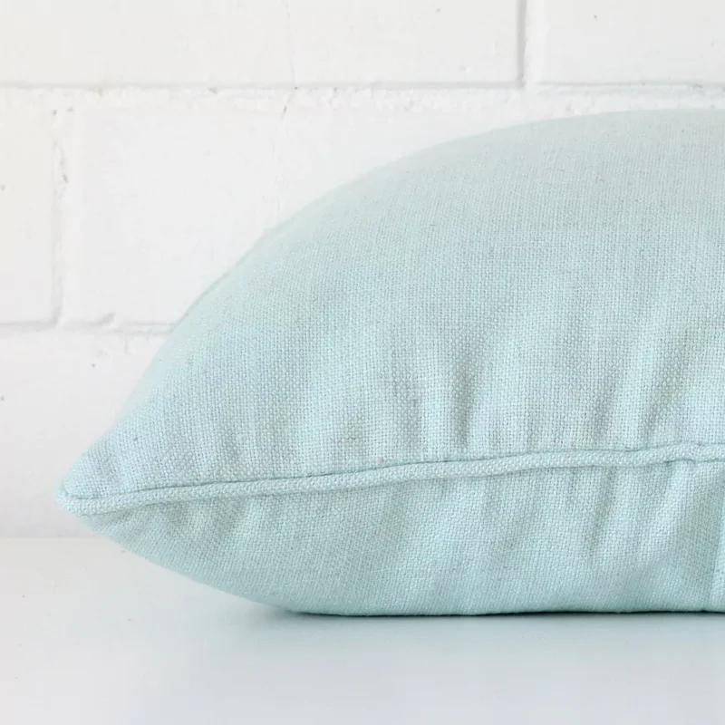 A square mint cushion cover laying flat. This viewpoint highlights the linen fabric from a side position.