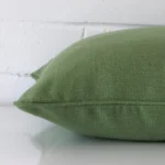 A green cushion positioned on its back panel. The shot shows a lateral view of the linen fabric and its square size.