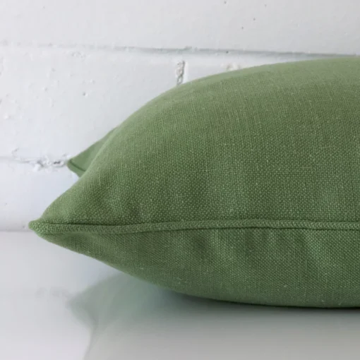 A green cushion positioned on its back panel. The shot shows a lateral view of the linen fabric and its square size.