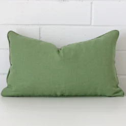 Sage green cushion leans elegantly against a brick wall. It has been crafted from a high quality linen material and has a rectangle shape.