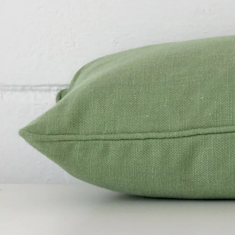 Side image of a linen rectangle cushion cover. The sage green colour is more visible from the side showing the attachment of the panels.