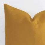 A very close image of the corner of a solid colour linen cushion.The finer detail of the square shape and mustard colour are visible.