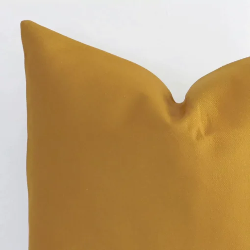 A very close image of the corner of a solid colour linen cushion.The finer detail of the square shape and mustard colour are visible.