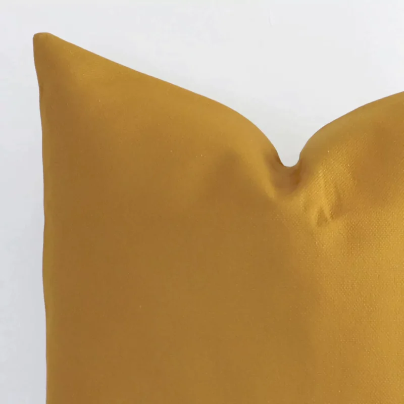 A very close image of the corner of a solid colour linen cushion.The finer detail of the square shape and mustard colour are visible.