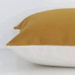 Horizontal edge of solid-coloured square cushion cover is shown. The linen fabric and mustard tone can be seen from this side view.