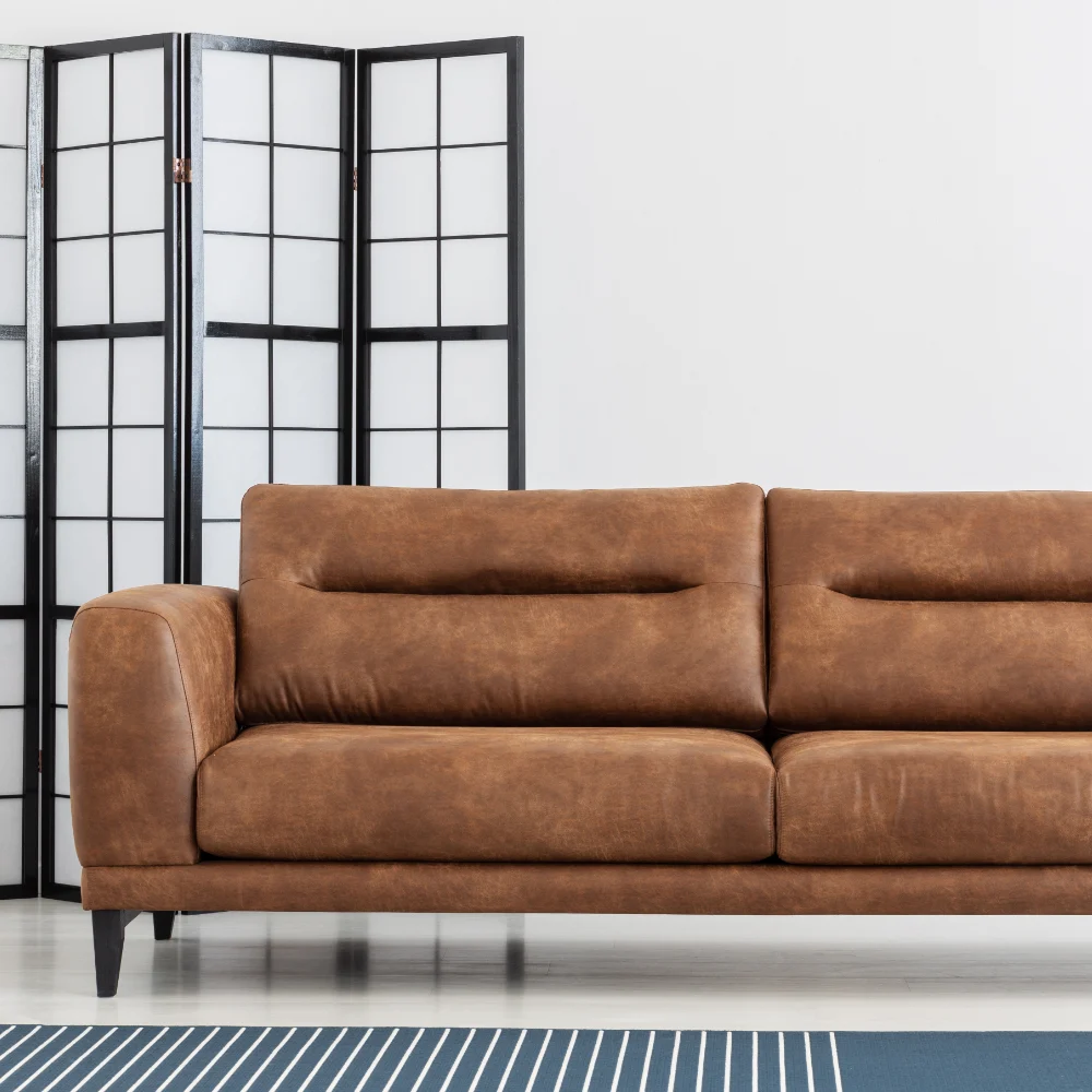 A minimalist room is shown with empty large leather seating. Perfect blank canvas for cushions for a brown sofa.