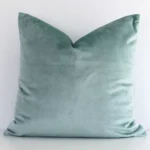Elegant square mint cushion positioned in front of white wall. Its solid colour style pops on the velvet fabric.
