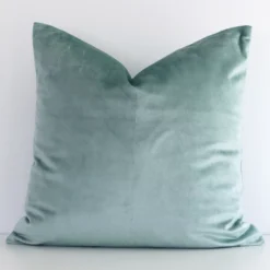 Elegant square mint cushion positioned in front of white wall. Its solid colour style pops on the velvet fabric.