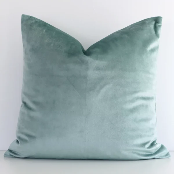 Elegant square mint cushion positioned in front of white wall. Its solid colour style pops on the velvet fabric.