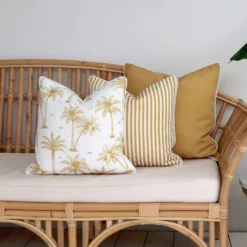 A rattan seat with 3 charming mustard-coloured outdoor couch cushions on it.